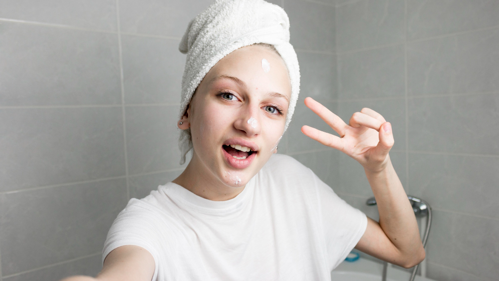 Teen girl with towel-wrapped hair applying acne cream during a simple skincare routine in the bathroom
